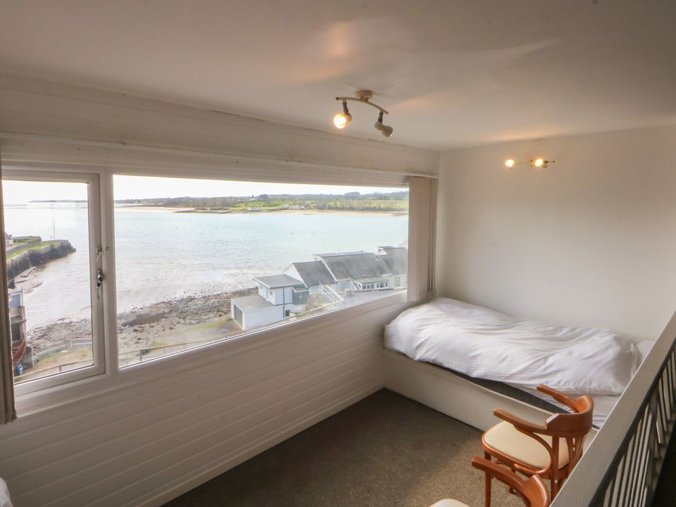 A bedroom with a bed and a chair overlooking the water at Seaview in Y Felinheli