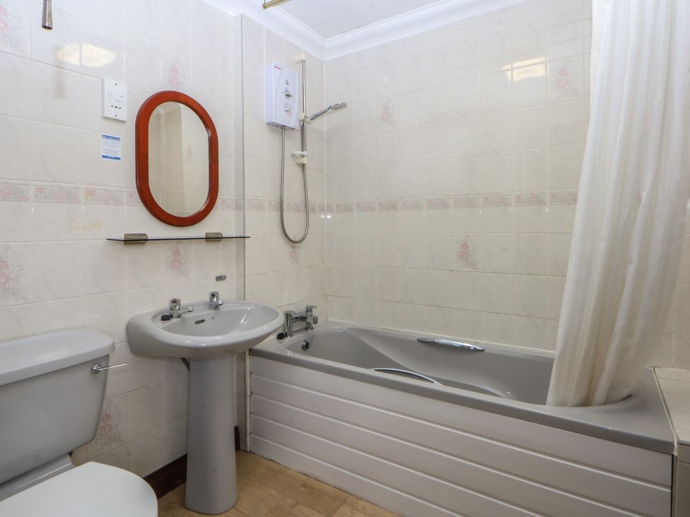 A bathroom with a bath tub, sink, toilet, and mirror at Seaview in Y Felinheli