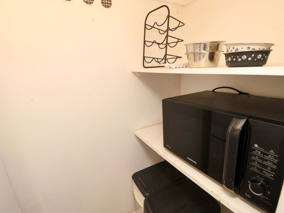 A kitchen with a microwave and storage shelves at Fern Cottage in Bembridge