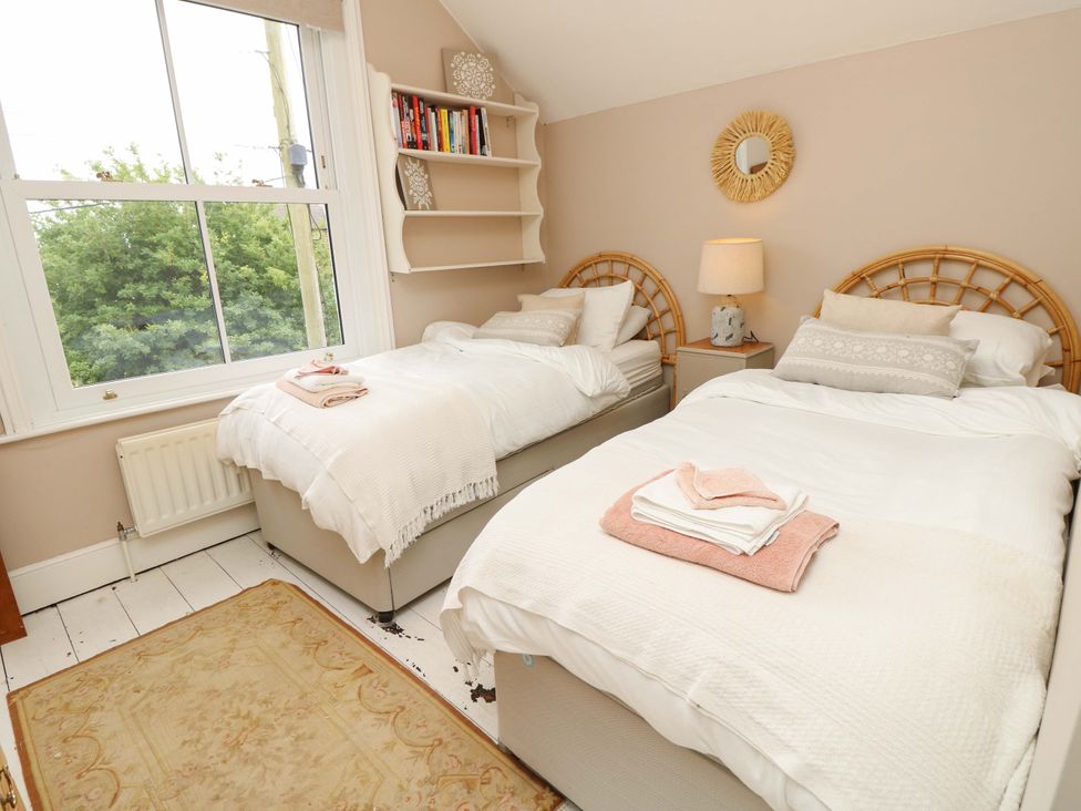 A bedroom with two beds and a bookshelf at Fern Cottage in Bembridge