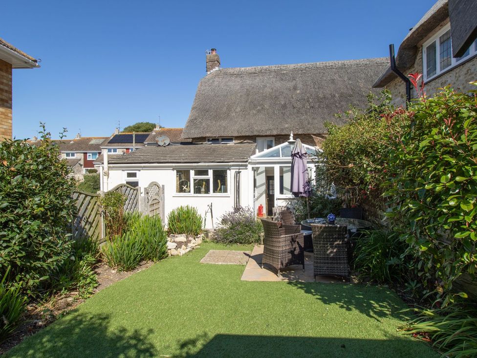 A garden with seating area and conservatory at Honeypot Cottage in Weymouth