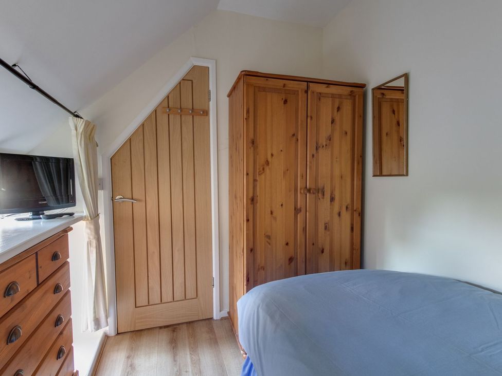 A bedroom with a bed, wardrobe, and television at Honeypot Cottage in Weymouth