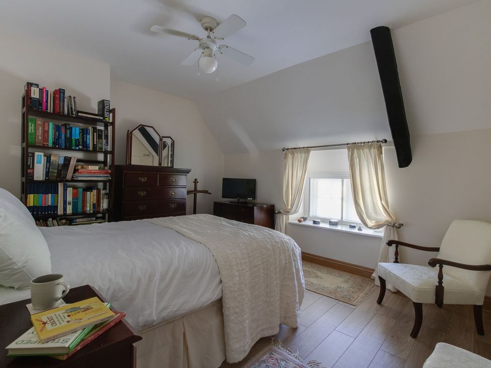 A bedroom with a bed, bookshelf, and a TV at Honeypot Cottage Weymouth