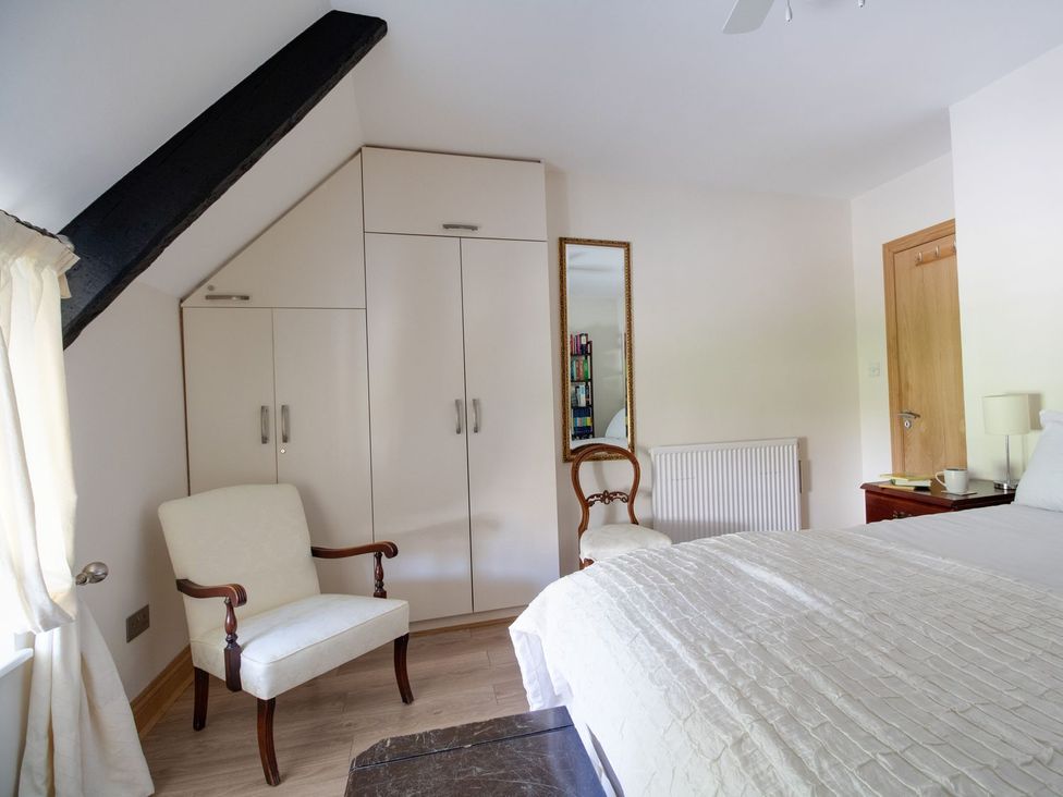 A bedroom with a bed, wardrobe and chairs at Honeypot Cottage in Weymouth