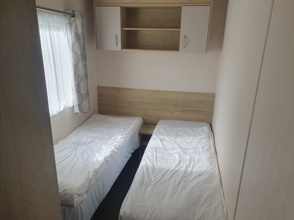 A bedroom with two single beds and a shelf at Caravan 325 in Lowestoft
