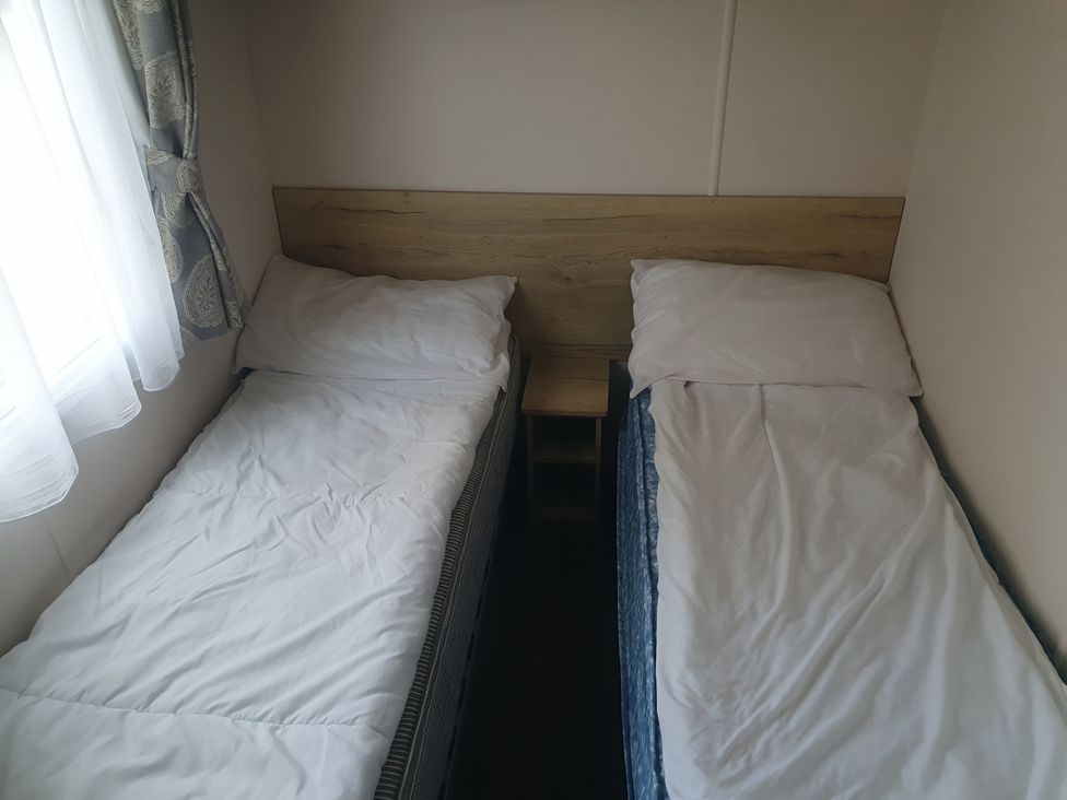 Two single beds with pillows and a bedside table at Caravan 325 in Lowestoft