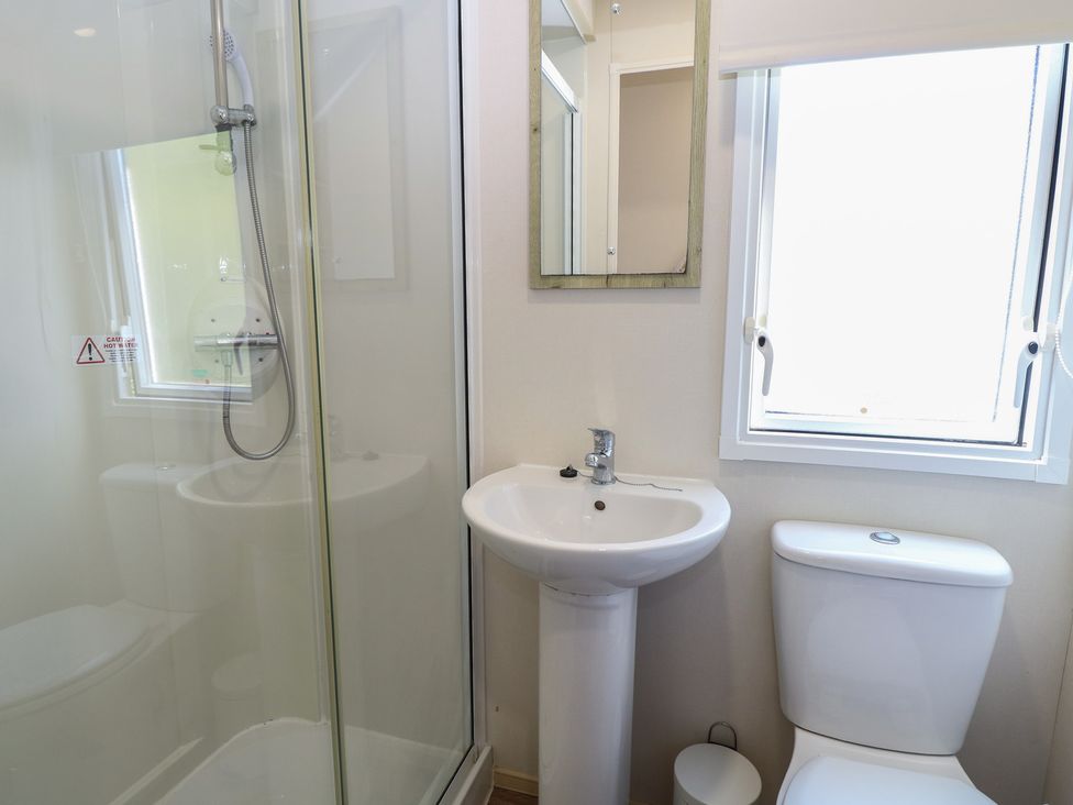 A bathroom with a shower, sink, toilet, and mirror at Caravan 325 in Corton
