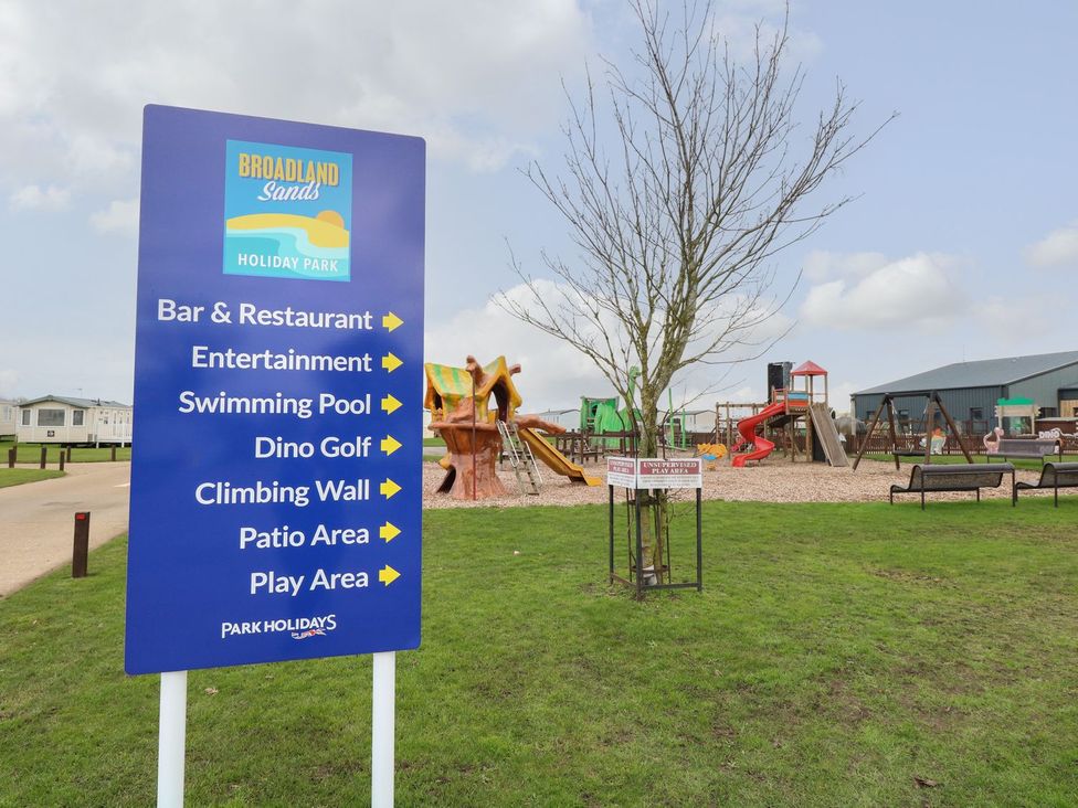A sign for Broadland Sands Holiday Park with playground equipment at Caravan 325 in Corton