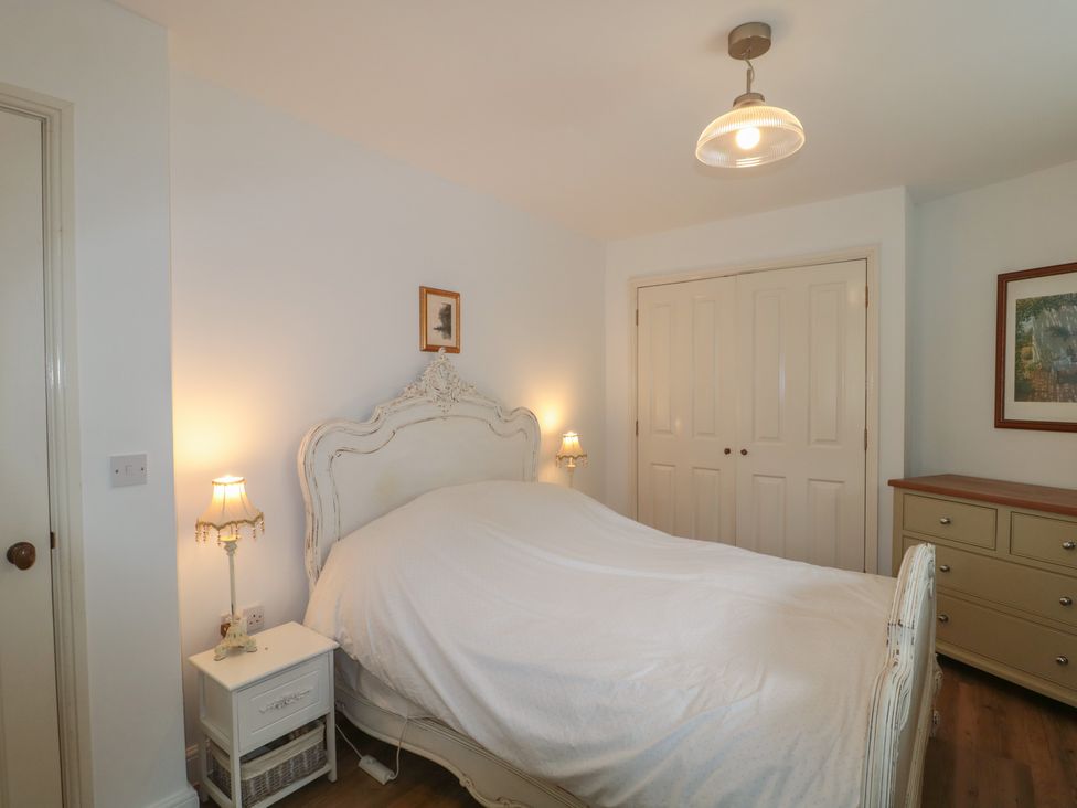 A bedroom with a bed, nightstand, lamp, and dresser at Longfords Mill near Nailsworth