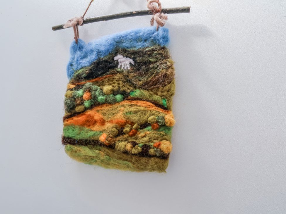 A felt artwork depicting a landscape hanging on a twig at 1 West Ville Mews York
