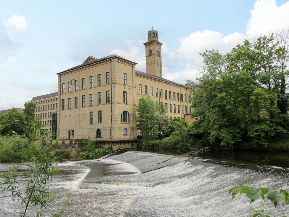 A building near a river with a waterfall and trees near Saltaire House in Saltaire