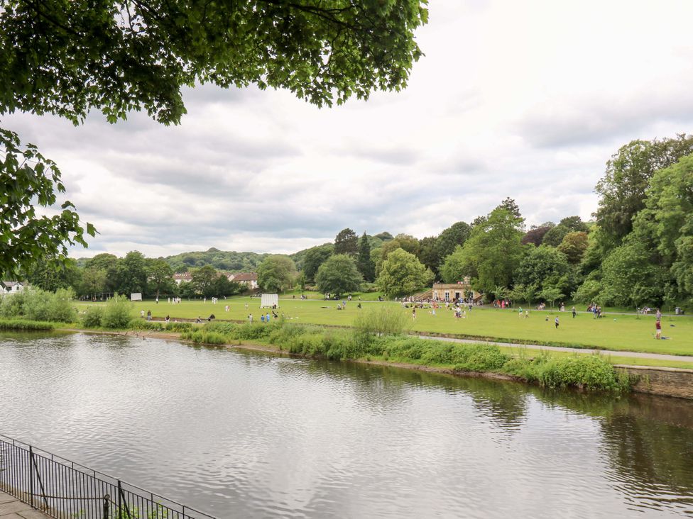 A park with people on grass and a river at Saltaire House in Saltaire