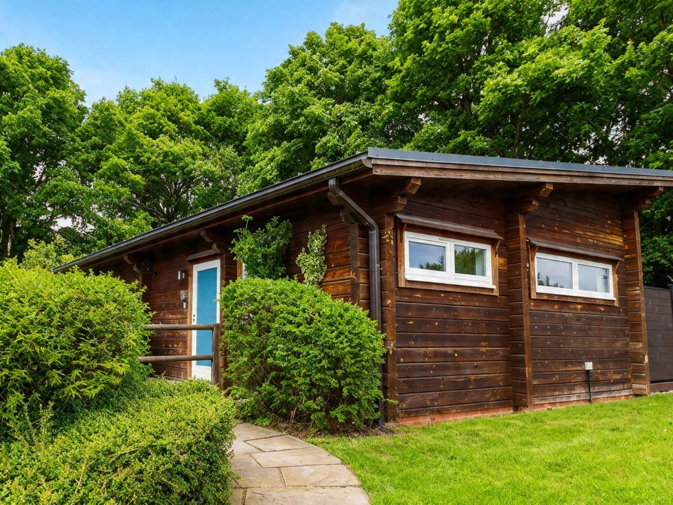 A wooden cabin with a blue door and small windows at Pine Lodge Spa Pet Thirsk