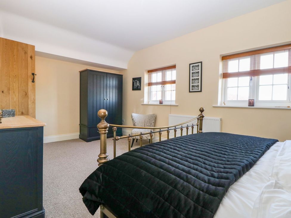 A bedroom with a bed, wardrobe, chair, and windows at Tuft House in Hovingham