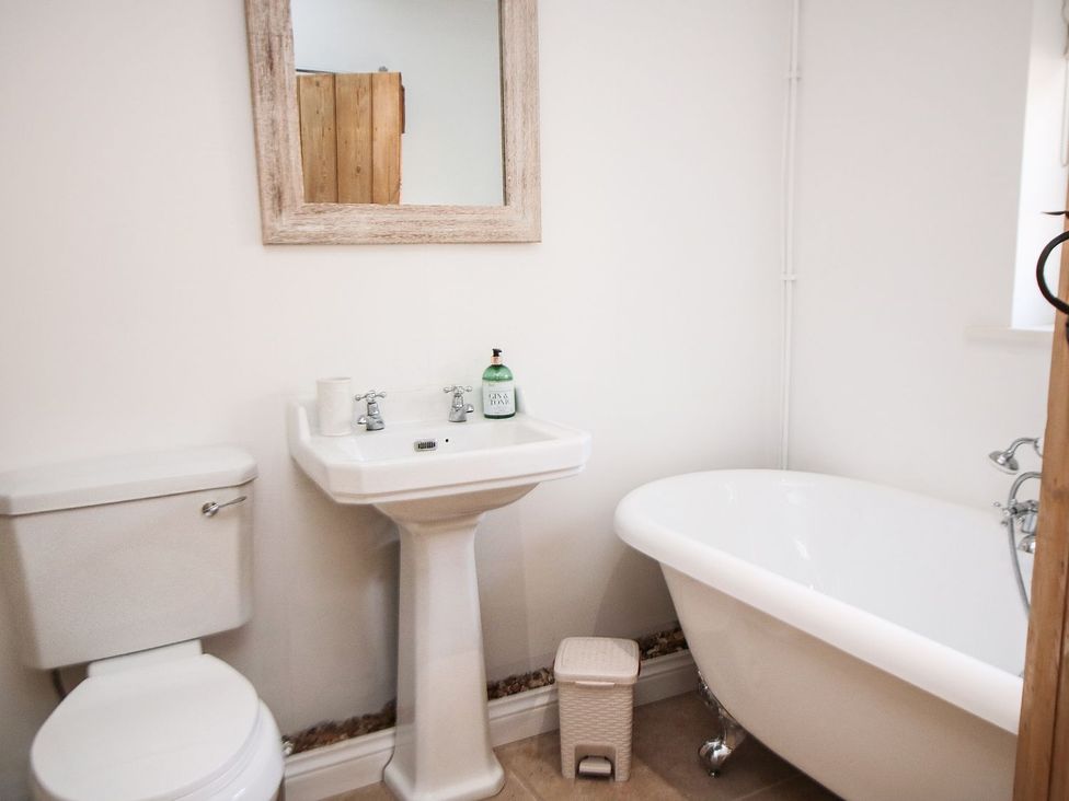 A bathroom with a toilet, sink, mirror, and bathtub at Tuft House in Hovingham