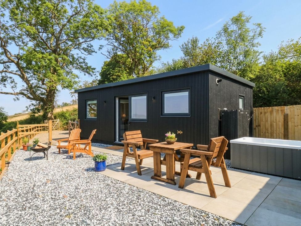 An outdoor area with a cabin, table, chairs, and hot tub at Little Folley in Whitestone near Tedburn St Mary