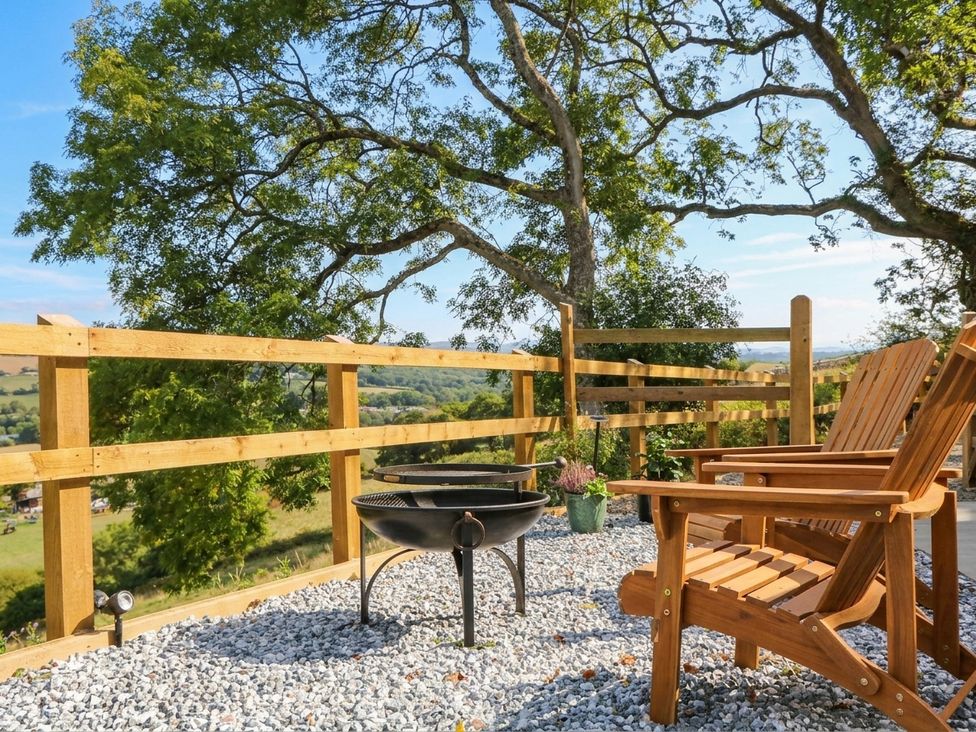 An outdoor seating area with wooden chairs and a fire pit at Little Folley Whitestone near Tedburn St Mary