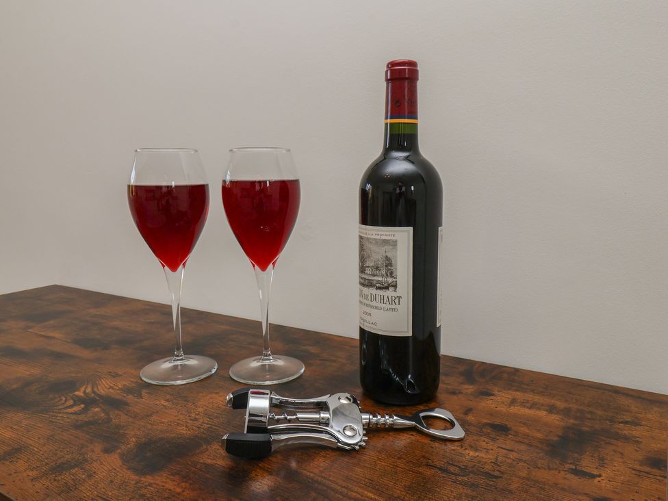 Two glasses of red wine with a bottle and corkscrew on a table at Helmsley Cottage in Helmsley