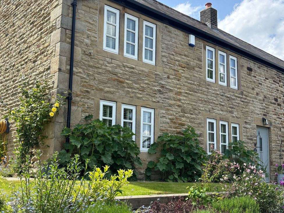 A stone house with multiple windows and garden plants at Holly Cottage in Totley