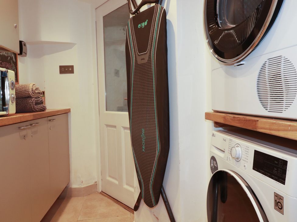 A laundry room with a washing machine and an ironing board at Dolphin Cottage in Falmouth