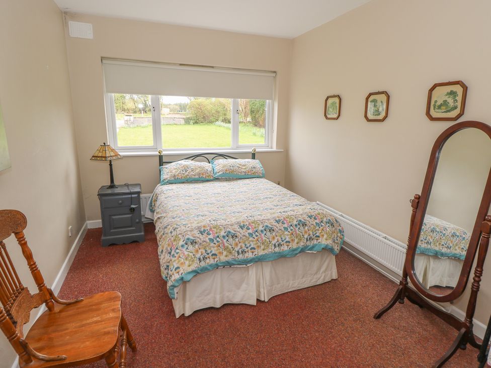 A bedroom with a bed, chair, lamp, and mirror at Sweetbriar Lodge in Castlerea