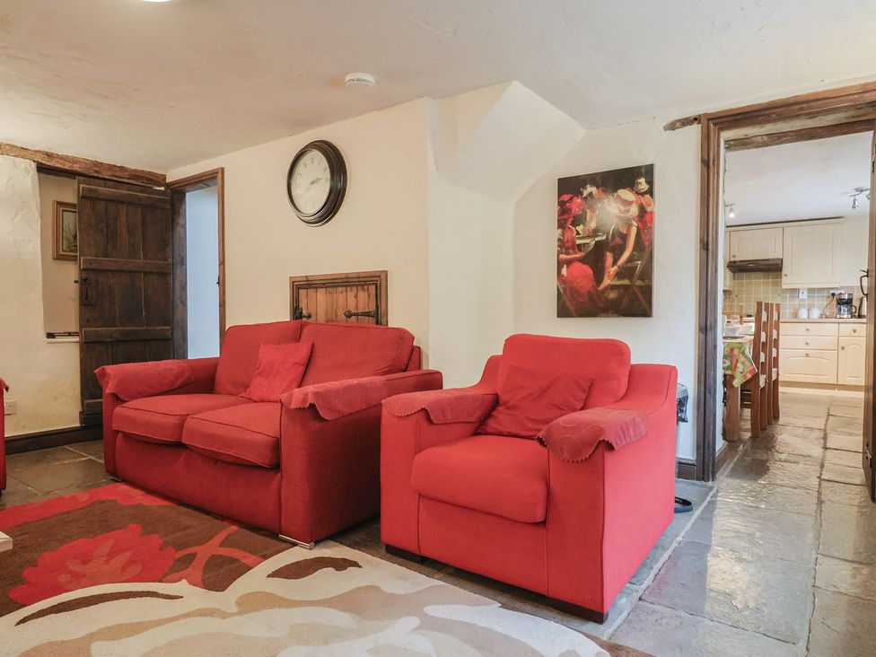 A living room with red sofas and a clock at Cider Cottage in Hawkchurch