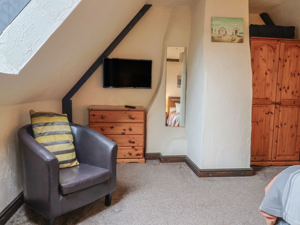 A bedroom with a television, armchair, chest of drawers, and wardrobe at Cider Cottage in Hawkchurch