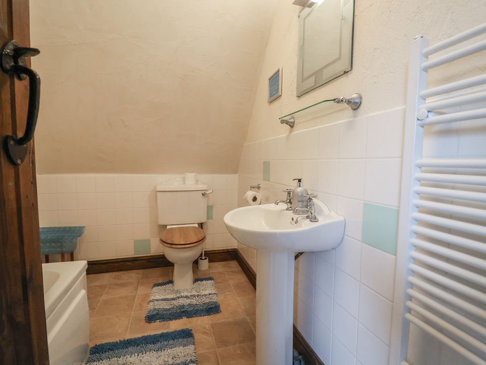 A bathroom with a toilet, sink, and mirror at Cider Cottage in Hawkchurch
