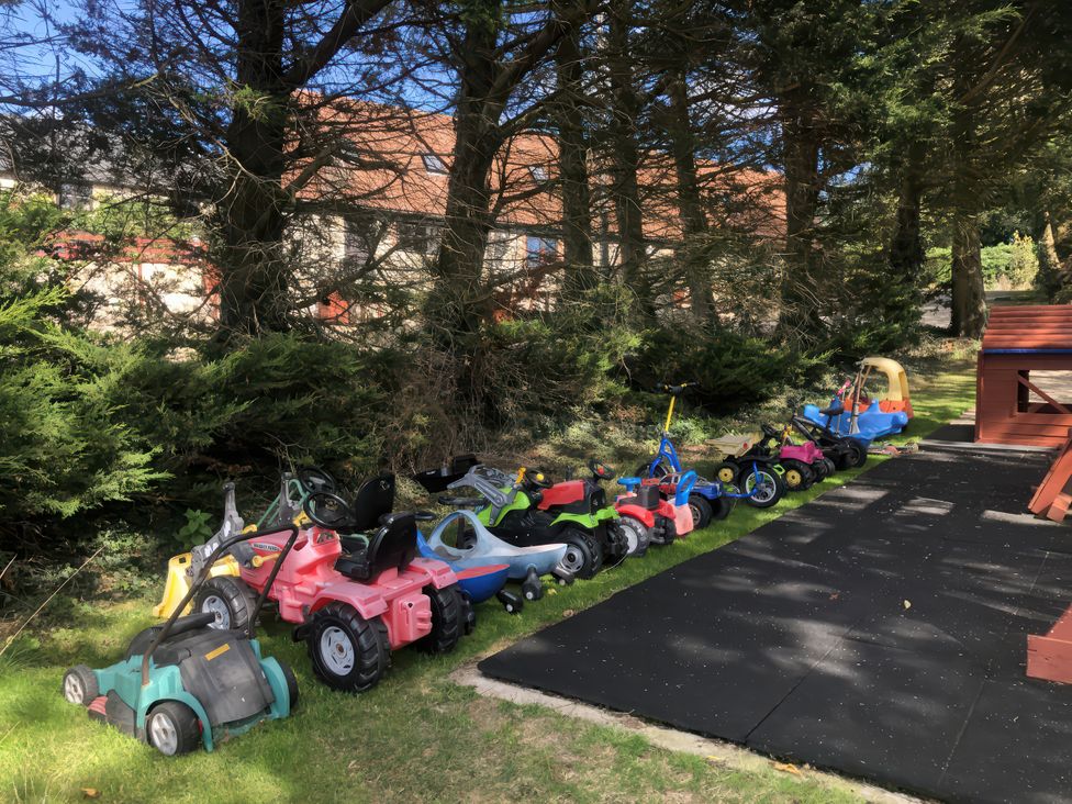 A row of children's tricycles and a playhouse in the garden at Cider Cottage in Hawkchurch