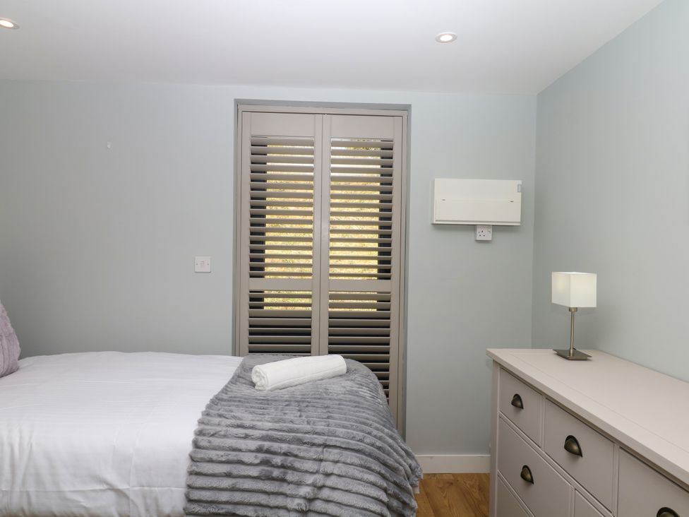 A bedroom with a bed, dresser, and window shutters at Fieldstone Barn North Tawton