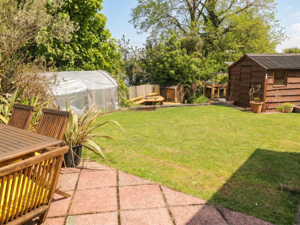 A garden with a table and chairs, greenhouse, and shed at 1 Rosemount Garden Villas Tenby
