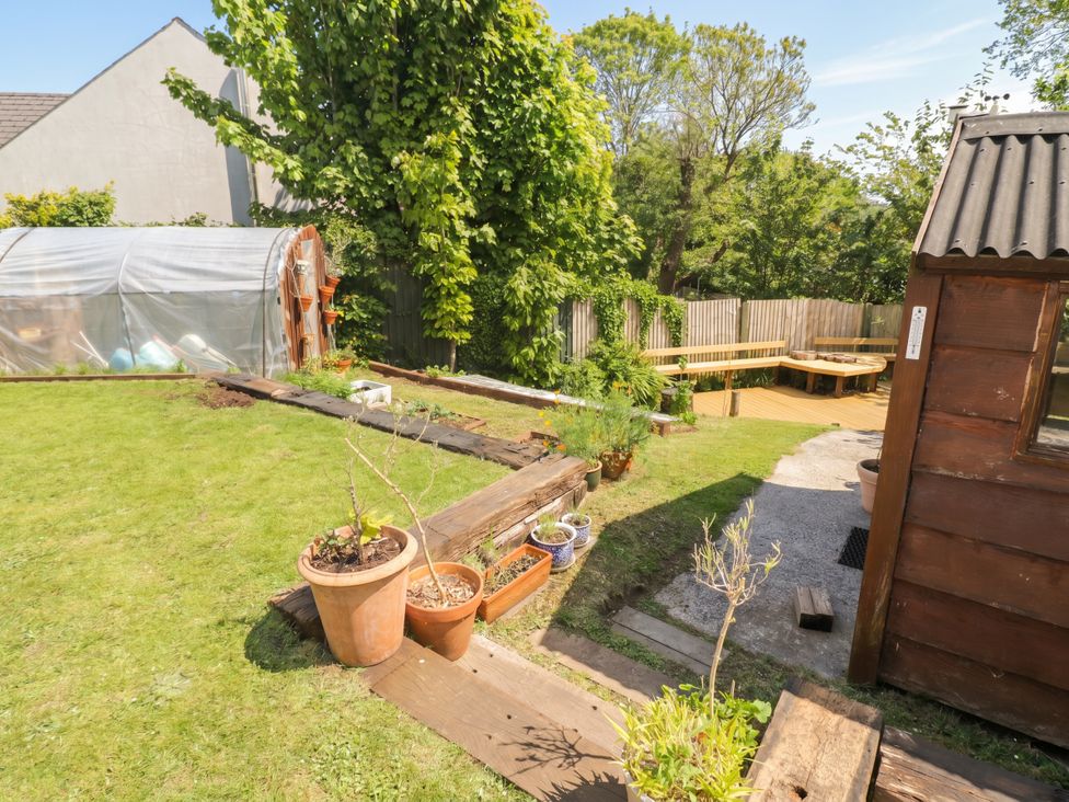 A garden with a greenhouse, wooden bench and pots at 1 Rosemount Garden Villas in Tenby