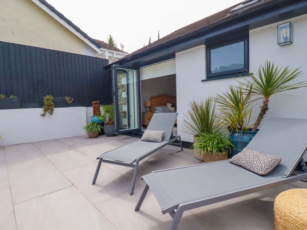 An outdoor patio with sun loungers and a glass door at No.45 Whealgolden Drive Newquay