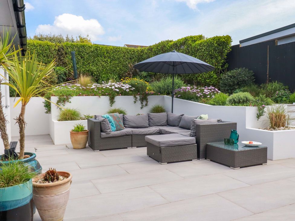 A garden with an outdoor sofa and umbrella at No.45 Whealgolden Drive in Newquay