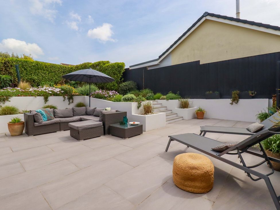 A garden with an outdoor sofa, umbrella, and planters at No.45 Whealgolden Drive Newquay