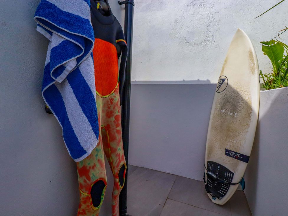 An outdoor shower area with a wetsuit and surfboard at No.45 Whealgolden Drive in Newquay