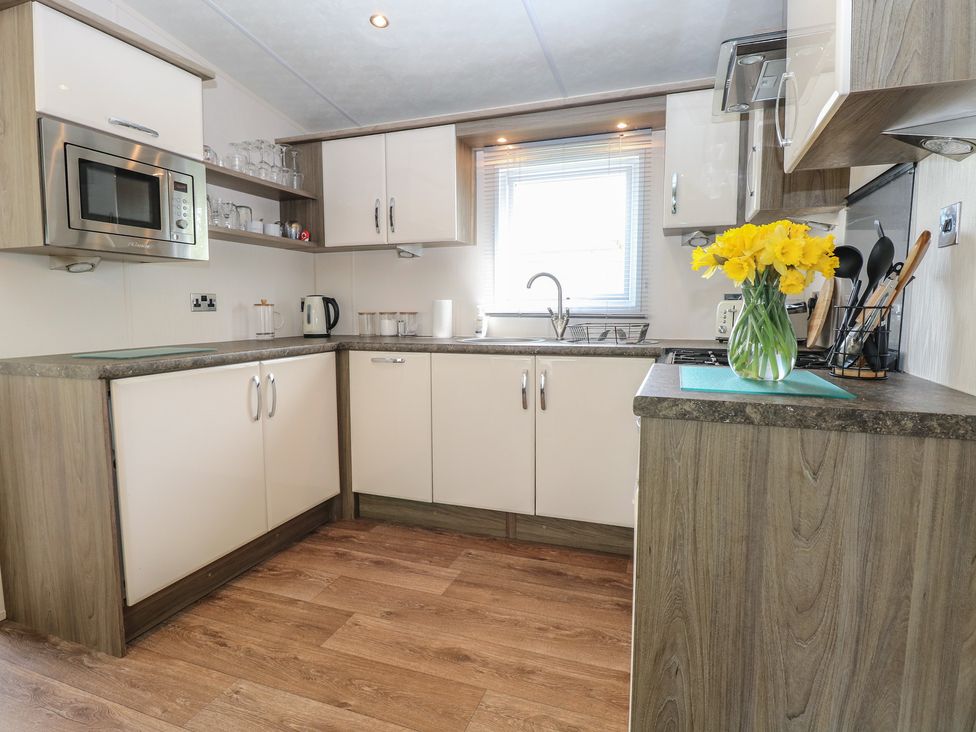 A kitchen with microwave, sink and flowers at The Norfolk Nook 18 Castle Walk Burgh Castle