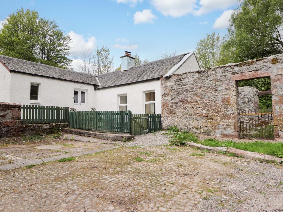 An outdoor area with a cottage and fence at Laundry Cottage in Strathpeffer