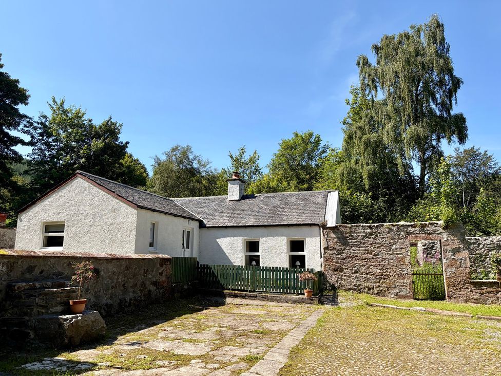 A house with a wall and trees at Laundry Cottage in Strathpeffer