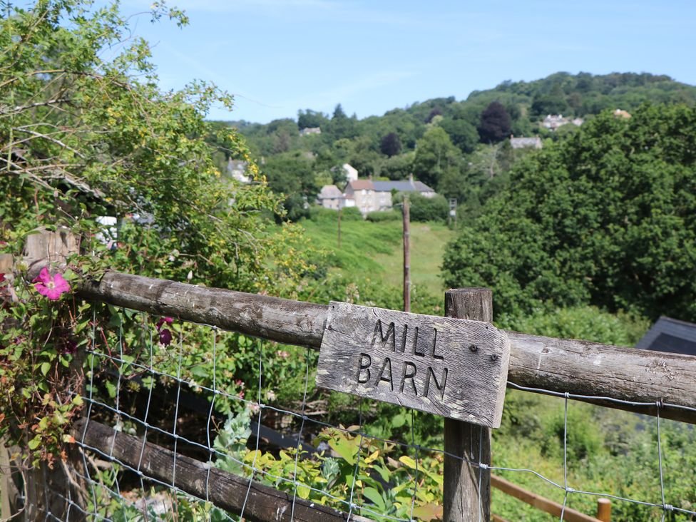 A sign on a fence indicating 'MILL BARN' with hills and trees in the background at The Mill Barn in Lustleigh