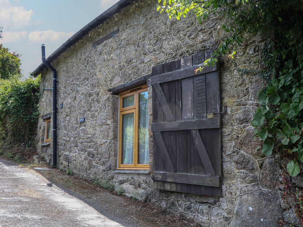 An exterior view of a stone cottage with a window and wooden shutters at The Mill Barn in Lustleigh