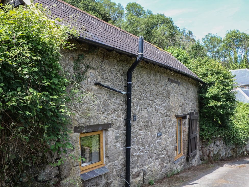 A stone building with windows and vegetation surrounding it at The Mill Barn in Lustleigh
