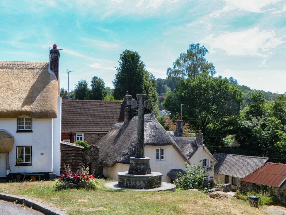 A view of a street with a stone monument and thatched roof houses at The Mill Barn in Lustleigh