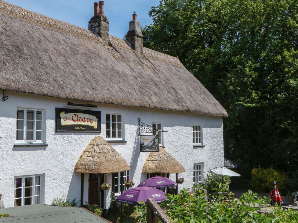 A public house building with a thatched roof and outdoor seating at The Cleave in Lustleigh