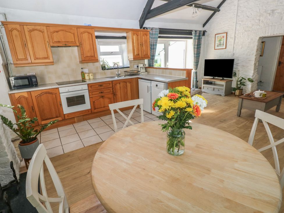 A kitchen with wooden cabinets and a dining table with flowers at Daffodil Cottage in Blaencwm near Treorchy