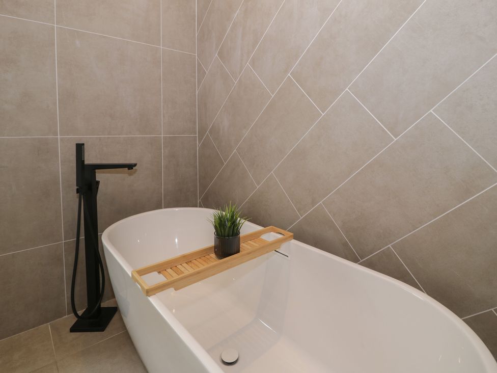 A bathroom featuring a bathtub with a wooden tray and plant at Llety Cllyd in Barmouth