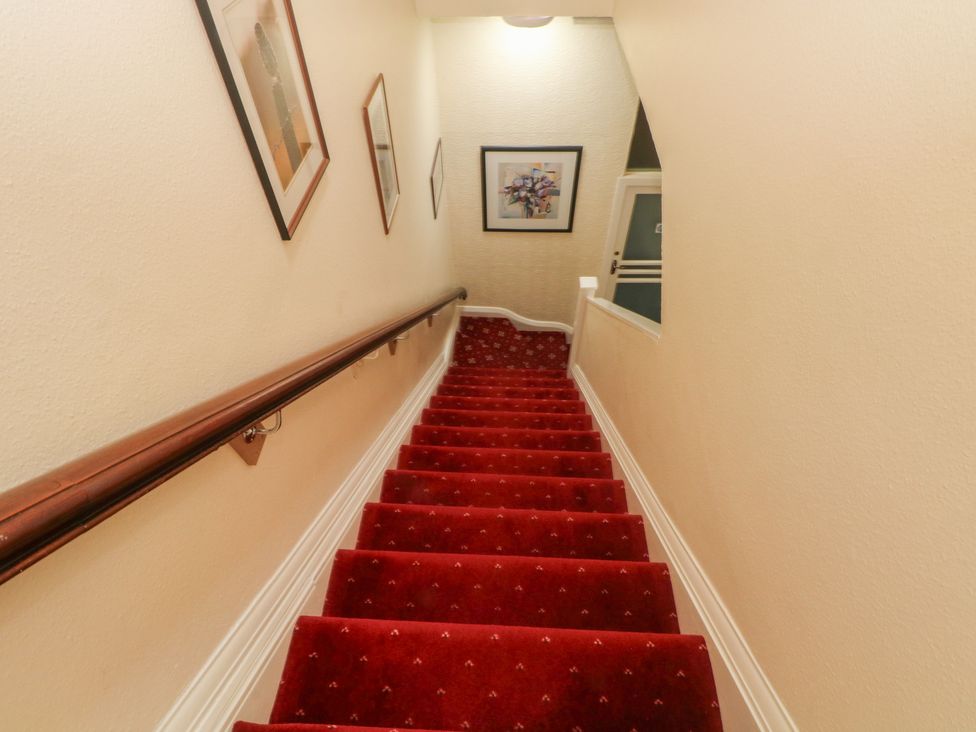 A staircase with red carpet and framed pictures at Apartment 3 in Lytham St. Annes