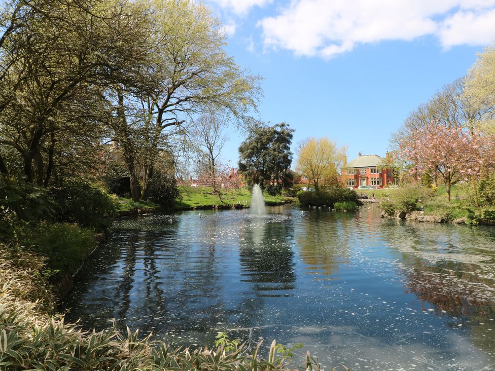 A pond with a fountain surrounded by trees and a building at Apartment 4 Lytham St. Annes