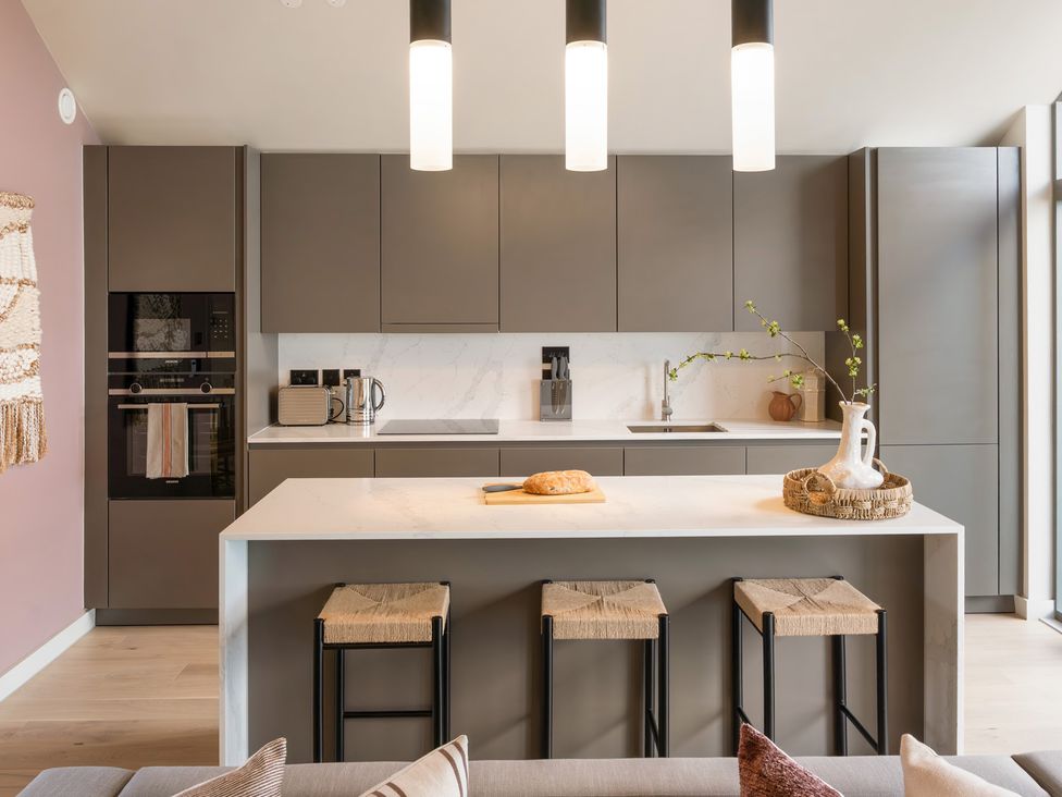 A kitchen with cabinets, island, sink, and stools at Clifftop House Hot Tub, St Ives