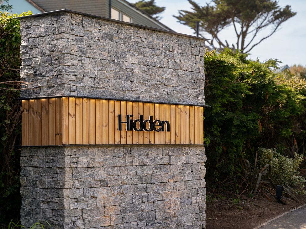A stone wall with a wooden sign at Hidden 18- St Ives Bay Suite Hot Tub in St Ives